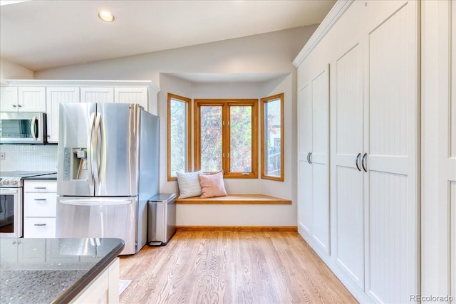 kitchen featuring appliances with stainless steel finishes, lofted ceiling, light wood-style flooring, white cabinetry, and dark stone counters