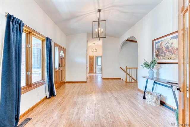 entryway with wood finished floors, a chandelier, baseboards, and arched walkways