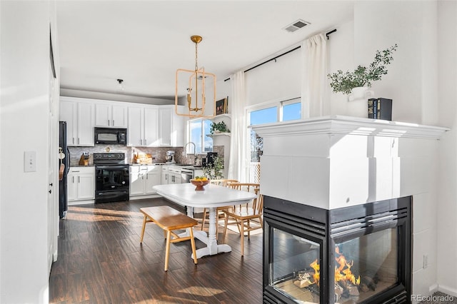 kitchen with pendant lighting, white cabinets, black appliances, dark hardwood / wood-style flooring, and tasteful backsplash