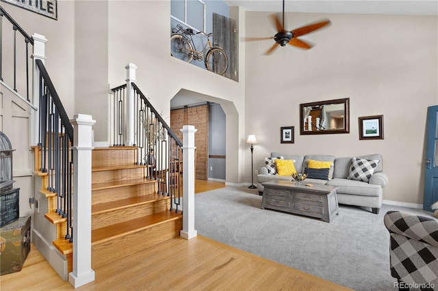 living room with ceiling fan, a high ceiling, and light wood-type flooring