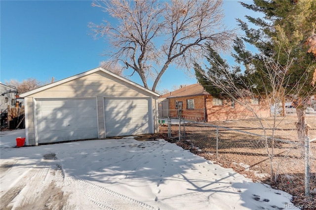 snow covered garage featuring a detached garage and fence