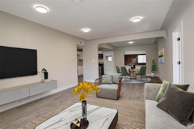 living area featuring arched walkways, baseboards, and wood finished floors