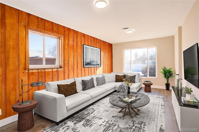 living area featuring visible vents, wooden walls, baseboards, and wood finished floors