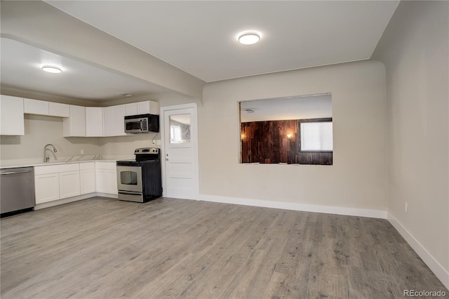 kitchen with stainless steel appliances, a sink, white cabinets, light countertops, and light wood-type flooring