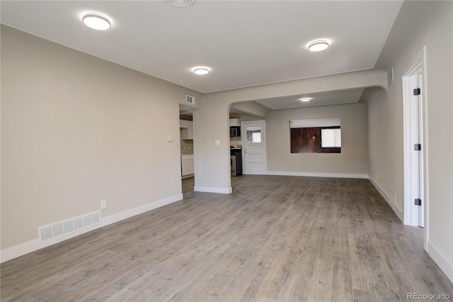 spare room featuring arched walkways, wood finished floors, visible vents, and baseboards