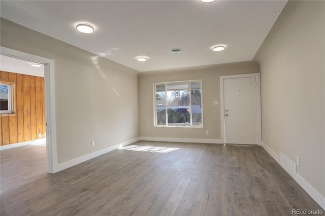 unfurnished room featuring visible vents, wooden walls, baseboards, and wood finished floors