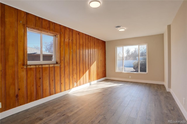 spare room featuring wood walls, visible vents, baseboards, and wood finished floors