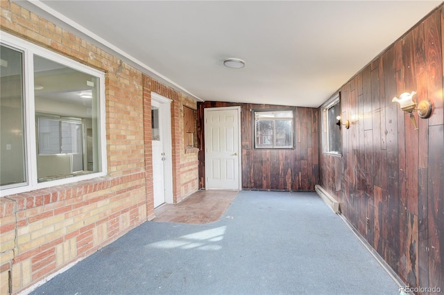 empty room with carpet floors, wood walls, and brick wall