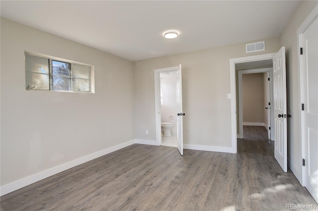 unfurnished bedroom with ensuite bathroom, wood finished floors, visible vents, and baseboards