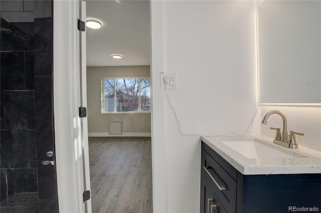 bathroom featuring baseboards, tiled shower, wood finished floors, and vanity