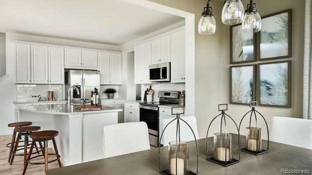 kitchen with stainless steel appliances, hanging light fixtures, a center island with sink, and white cabinets