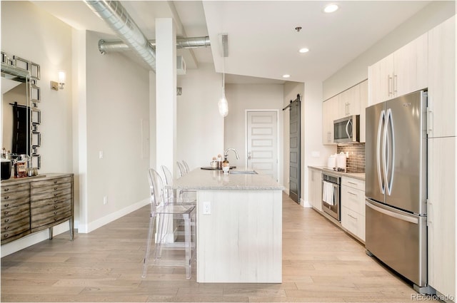 3198 Blake St Unit 502, Denver, CO 80205 - kitchen featuring stainless steel appliances, a barn door, a kitchen breakfast bar, light wood-style flooring, and tasteful backsplash