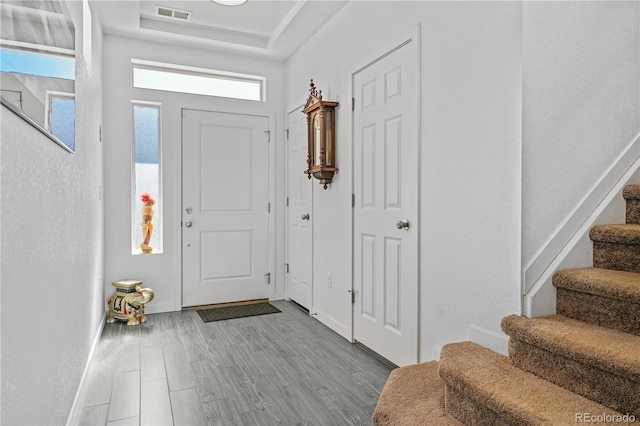 entrance foyer with visible vents, baseboards, stairs, light wood-style floors, and a raised ceiling