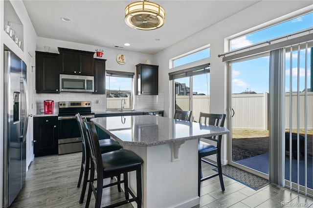 kitchen featuring appliances with stainless steel finishes, a breakfast bar, a center island, dark cabinetry, and backsplash