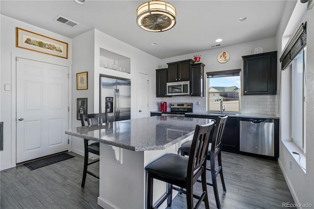 kitchen featuring a breakfast bar, stainless steel appliances, backsplash, a sink, and a kitchen island