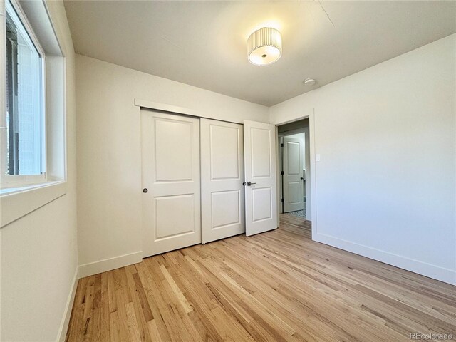 unfurnished bedroom with a closet, light wood-style flooring, and baseboards