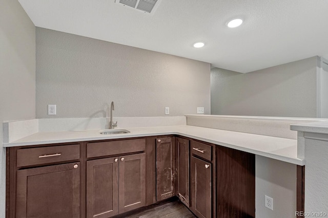 kitchen featuring kitchen peninsula, dark hardwood / wood-style flooring, dark brown cabinetry, and sink