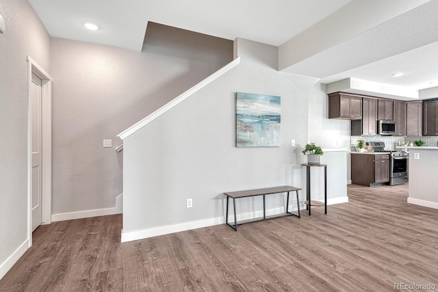 kitchen with decorative backsplash, dark brown cabinets, stainless steel appliances, and light hardwood / wood-style floors