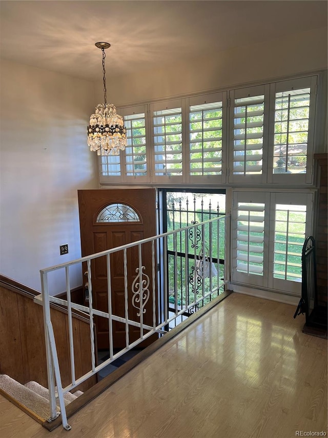 hall featuring a notable chandelier, a healthy amount of sunlight, wood-type flooring, and wood walls