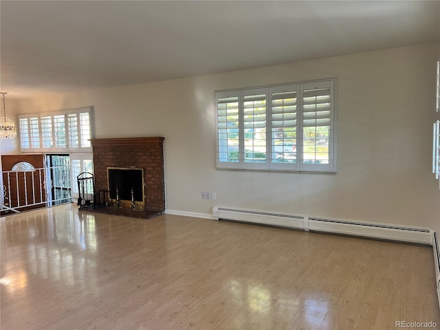 unfurnished living room with a notable chandelier, a baseboard heating unit, wood-type flooring, and a brick fireplace