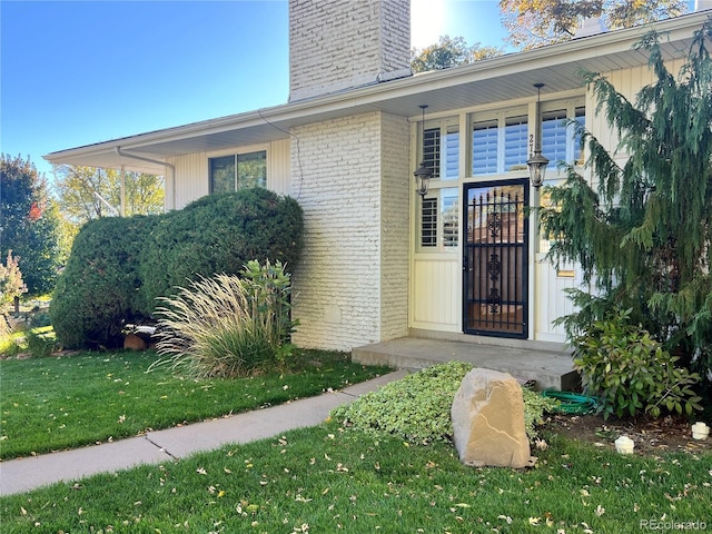 2789 S Ivan Way, Denver, CO 80227 - view of exterior entry with a chimney, brick siding, and a lawn