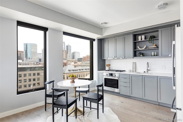 kitchen featuring gray cabinets, decorative backsplash, light hardwood / wood-style floors, and stainless steel appliances