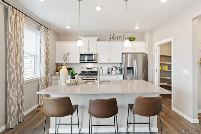 kitchen featuring appliances with stainless steel finishes, decorative light fixtures, an island with sink, and white cabinetry