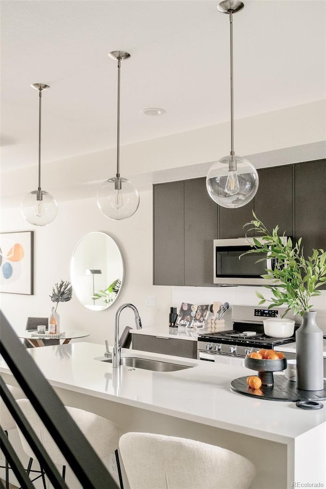 kitchen featuring stainless steel appliances, light countertops, decorative light fixtures, and a sink