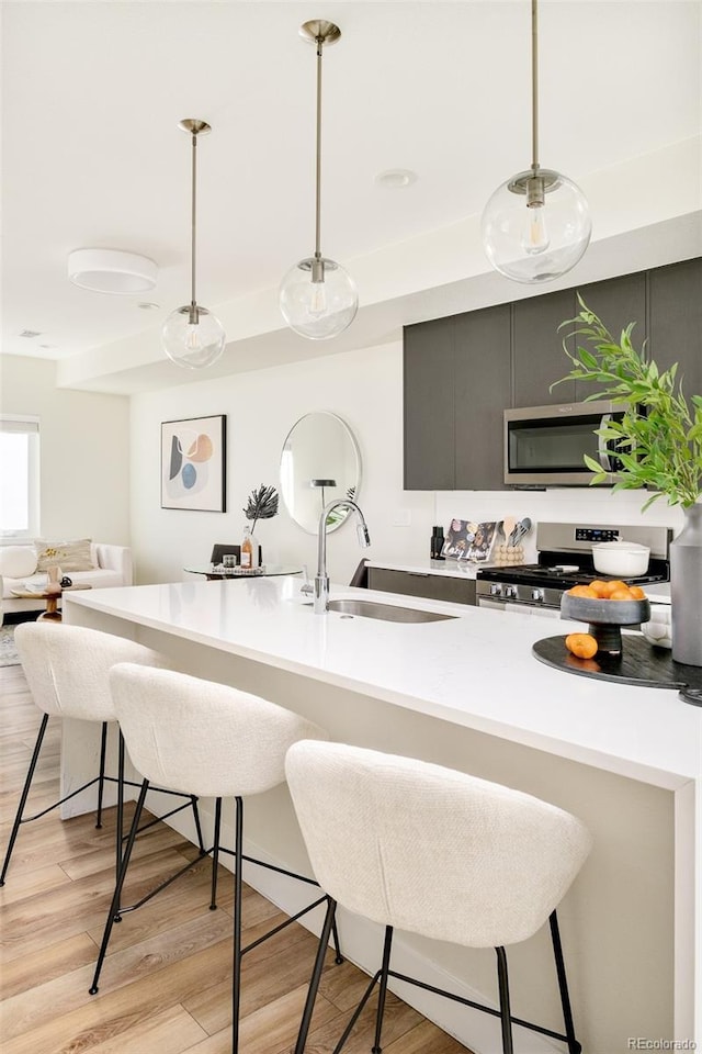 kitchen featuring decorative light fixtures, light wood finished floors, stainless steel appliances, a sink, and a kitchen breakfast bar