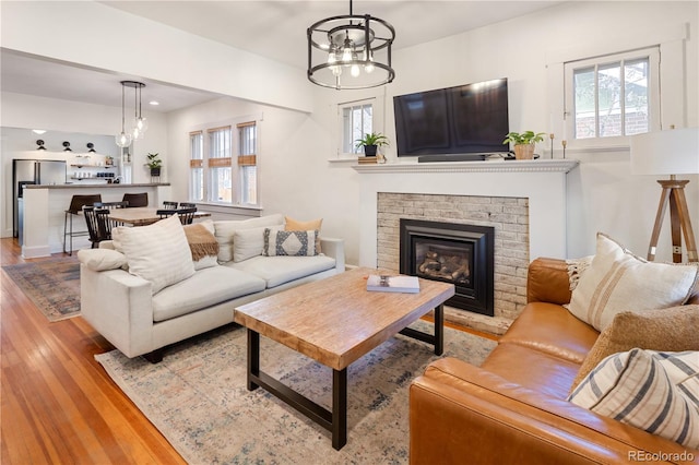 living area featuring a wealth of natural light, a brick fireplace, light wood-style flooring, and a notable chandelier