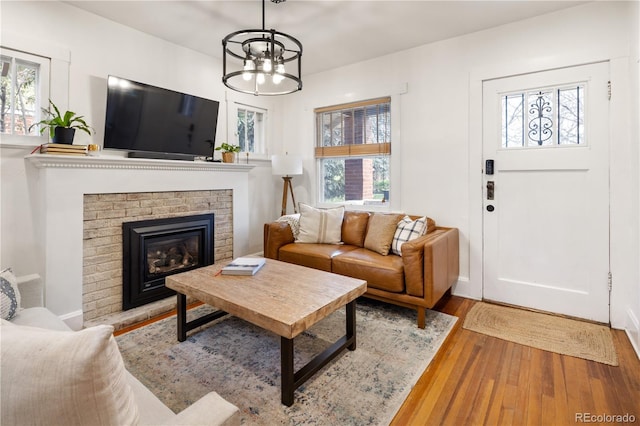 living room with a brick fireplace, a chandelier, plenty of natural light, and wood finished floors