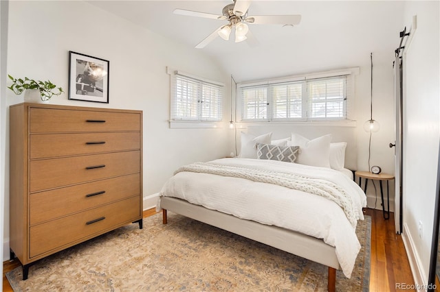 bedroom with ceiling fan, vaulted ceiling, a barn door, baseboards, and light wood-style flooring
