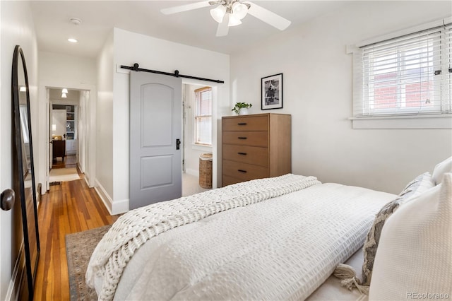 bedroom featuring baseboards, a barn door, wood finished floors, and multiple windows