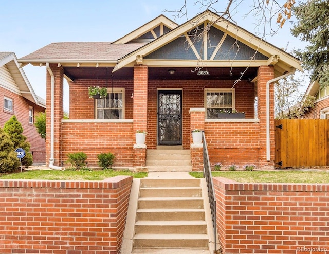 view of front facade with fence, covered porch, and brick siding