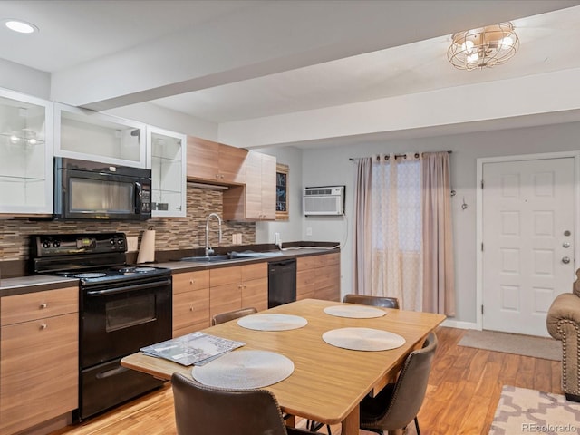 kitchen featuring sink, a wall unit AC, tasteful backsplash, black appliances, and light hardwood / wood-style floors