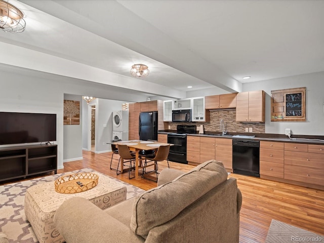 living room with light hardwood / wood-style floors, sink, beamed ceiling, and stacked washer and dryer