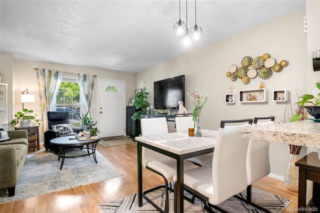 dining area featuring a textured ceiling, baseboards, and light wood-style floors