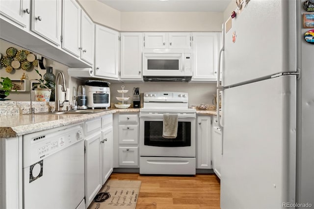 kitchen featuring white appliances, a sink, white cabinets, light wood-style floors, and light stone countertops