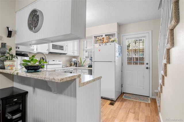 kitchen with light wood-style flooring, white cabinetry, a healthy amount of sunlight, white appliances, and a peninsula