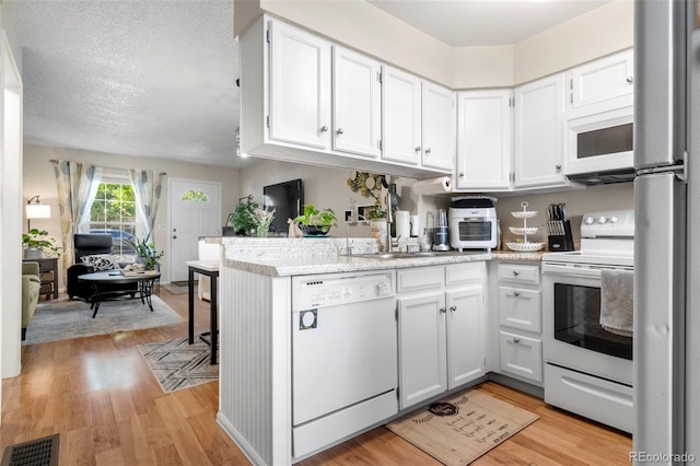 kitchen featuring a peninsula, white appliances, visible vents, and white cabinets