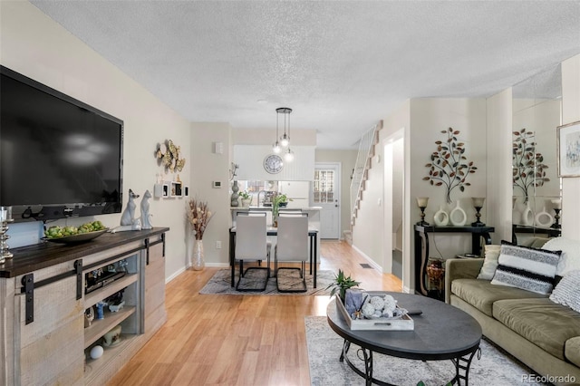 living area with a textured ceiling, light wood finished floors, stairway, and baseboards