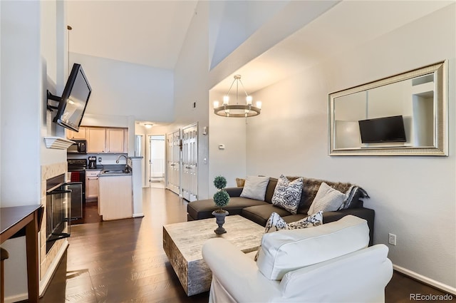 living room with dark wood-style floors, a chandelier, high vaulted ceiling, and baseboards