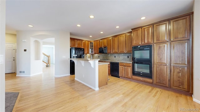 kitchen with black appliances, an island with sink, decorative backsplash, a kitchen breakfast bar, and light wood-type flooring