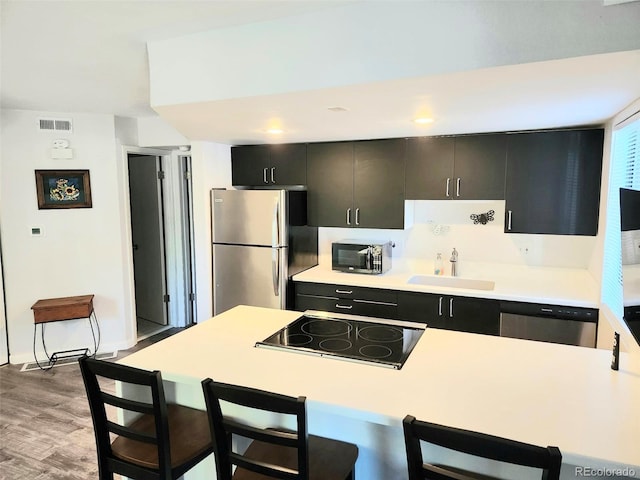 kitchen featuring a kitchen bar, stainless steel appliances, sink, and light hardwood / wood-style flooring