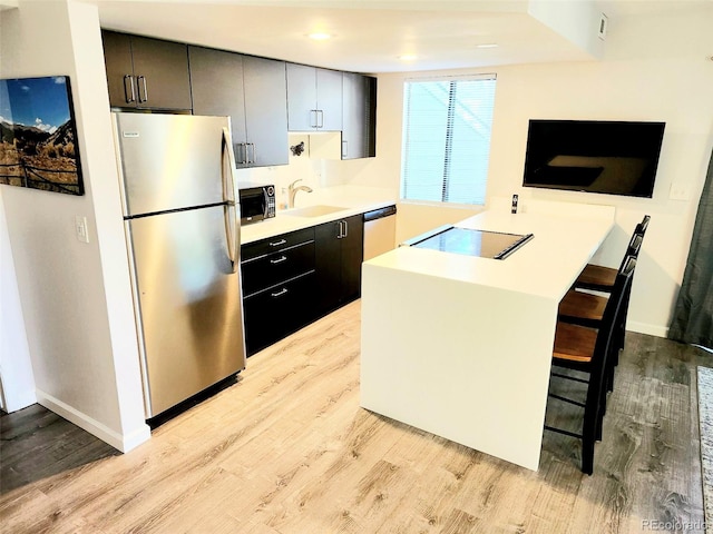 kitchen with a breakfast bar, light hardwood / wood-style floors, sink, kitchen peninsula, and stainless steel appliances