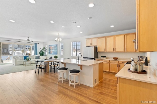 kitchen featuring sink, fridge, a wealth of natural light, an island with sink, and light brown cabinets