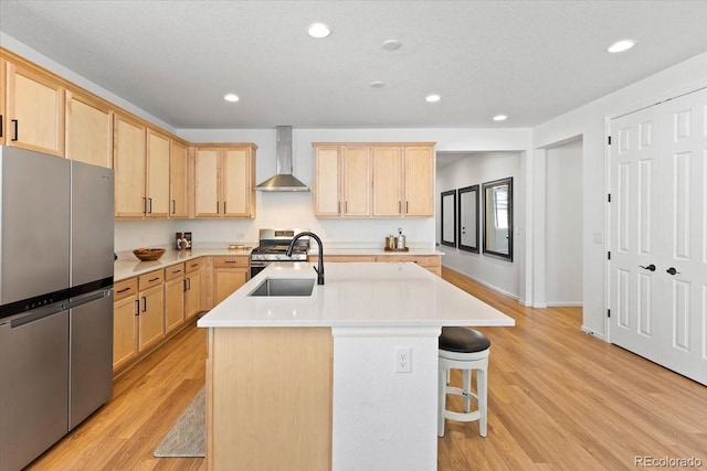 kitchen featuring stainless steel appliances, a center island with sink, light brown cabinets, and wall chimney exhaust hood