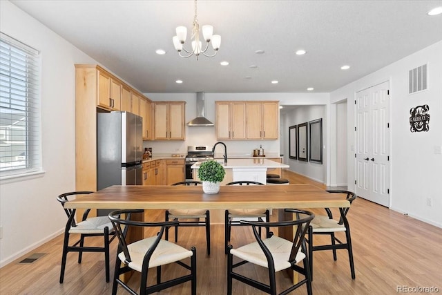 kitchen with a healthy amount of sunlight, wall chimney exhaust hood, stainless steel appliances, and light brown cabinetry