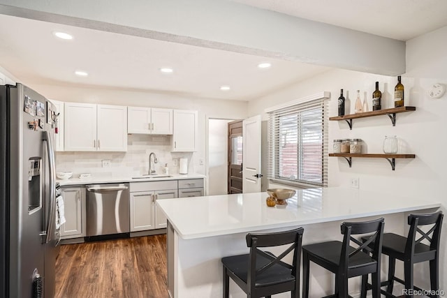 kitchen featuring sink, dark hardwood / wood-style flooring, kitchen peninsula, white cabinets, and appliances with stainless steel finishes