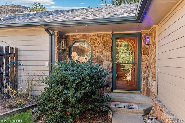 doorway to property with stone siding and a shingled roof